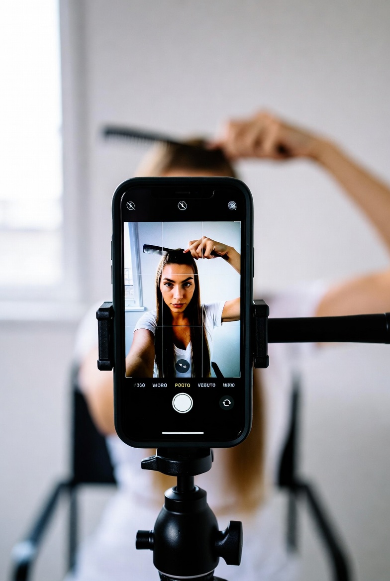 Person filming themselves doing hair routine with phone on tripod